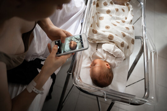 Mother photographing newborn baby in hospital bassinet