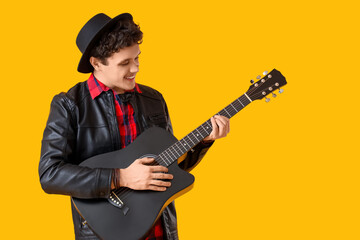 Young happy man playing new black guitar on yellow background
