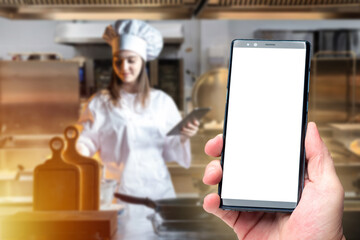 Restaurant, food service. Chef in professional kitchen prepares meal while using tablet, smartphone...