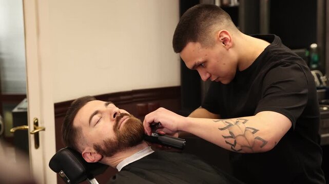 Stylist trimming man's beard with hair clipper in barbershop