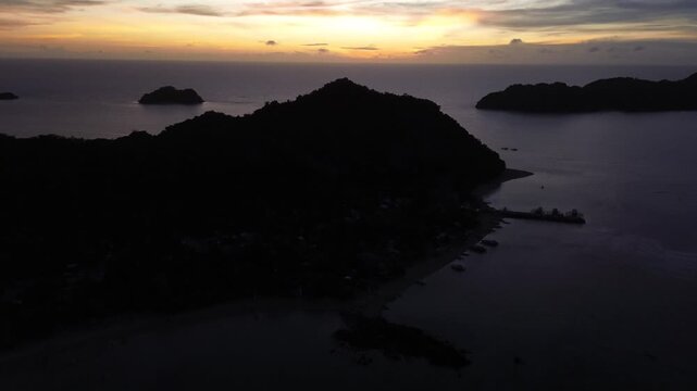 Cinematic drone flight over Guimaras Island in the Philippines at sunrise. The camera moves forward above the tropical island landscape, heading toward glowing sun on the horizon. Warm golden light.