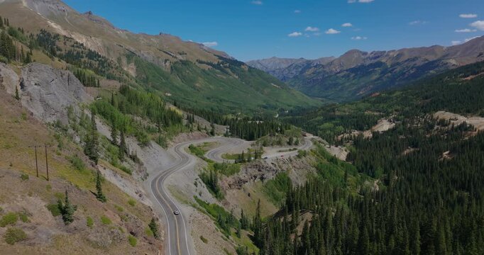 Broad aerial of alpine valley with mountain highway stretching by Colorado wilderness, Million Dollay Highway Colorado USA