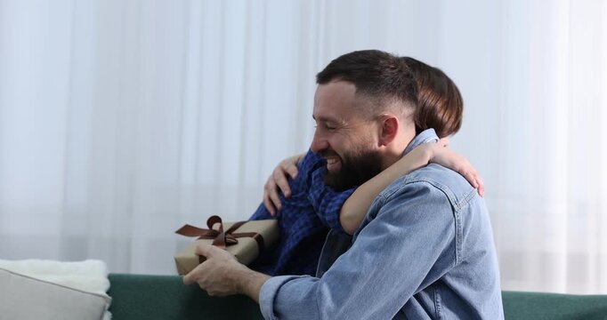 Cute boy surprising his father with gift at home
