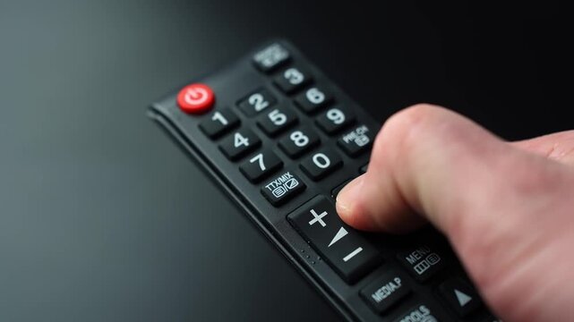 Close-up of a hand pressing the menu button on a TV remote control on a dark background, shallow depth of field&mdash;perfect for streaming, settings, navigation, and home entertainment themes.