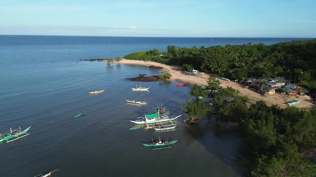 High-angle drone shot over the coastal mangrove area of Guimaras Island, Philippines. Turquoise tropical waters surround dense green mangrove vegetation, while small traditional banca boats float near