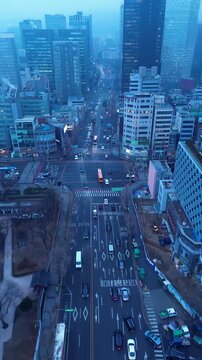 Drone aerial portrait of car vehicles and transport traffic driving through busy street intersection with urban city skyline buildings in background Jongno 3-ga Seoul South Korea Asia travel tourism