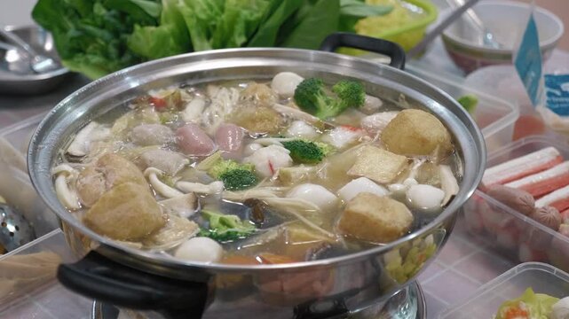 High-angle shot of a bubbling hot pot filled with fresh vegetables and seafood balls during a festive Lunar New Year family gathering.