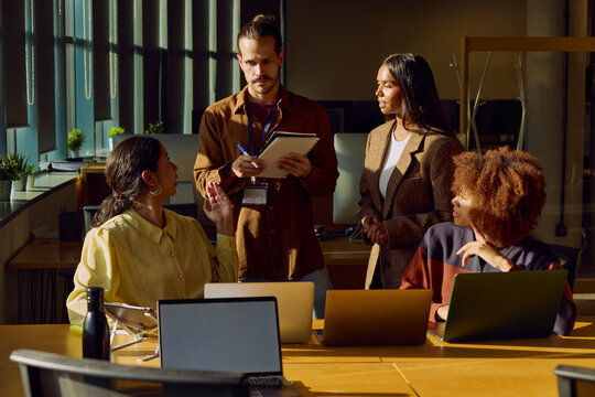 Coworkers discussing work around laptops in office meeting