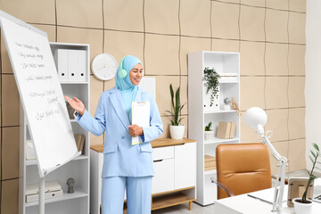 Obraz premium Young Muslim businesswoman with headphones learning Arabic language near flipchart in office