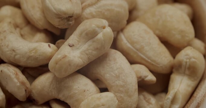 Close-up of a hand picking up fresh cashew nuts from a small wooden bowl, a healthy and nutritious snack concept isolated on a white background filmed in slow motion for a dramatic effect