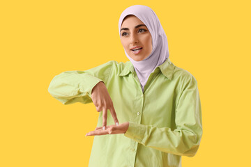 Beautiful Muslim deaf mute woman using sign language on yellow background © Pixel-Shot