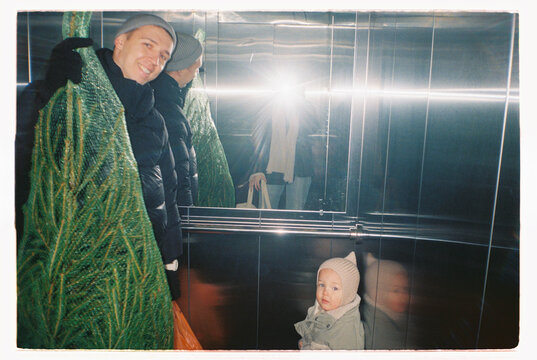 Family with toddler and Christmas tree inside elevator on analog film