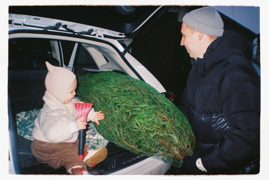 Family loading Christmas tree into a car with a toddler on analog film