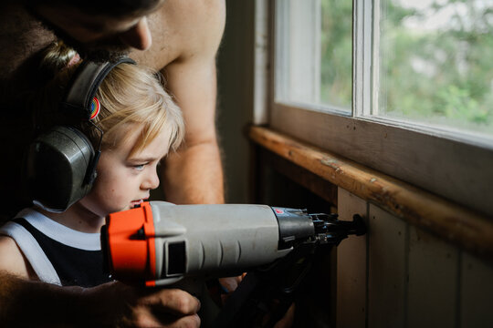 Young girl guided by her father in using nail gun 