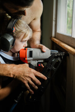 Young girl guided by her father in using nail gun 