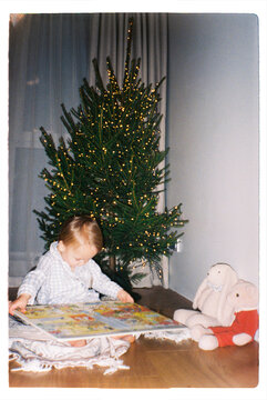 Toddler reading book on the floor near a Christmas tree at home