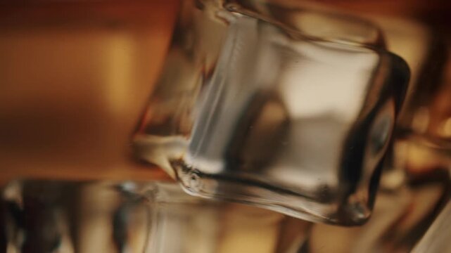 Close up of an elegant glass of golden brown whiskey with ice cubes swirling around in slow motion, creating mesmerizing ripples on the surface against a beautiful golden bokeh background