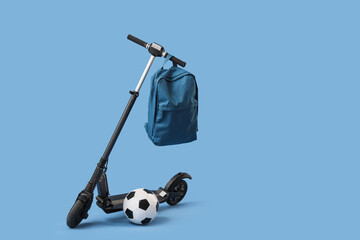 Modern electric scooter with backpack and soccer ball on blue background