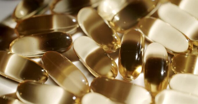 Many shiny golden fish oil capsules, containing omega-3 fatty acids for health and wellness, rotating on a white background. Golden fish oil omega 3 capsules rotating.
