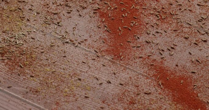 Red paprika powder and cumin seeds getting blown away by a gust of wind from a rustic wooden surface, beautiful dynamic texture of mixed exotic spices. Wind blowing away paprika and cumin spices