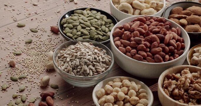 Assortment of healthy nuts and seeds in bowls on a wooden background, representing a source of vitamins and nutrients for a balanced diet, showcasing a variety of vegan protein snacks