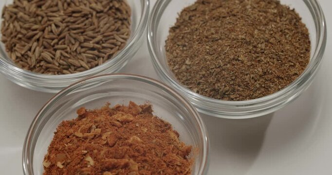 Various oriental spices like cumin, paprika, Aromatic cumin seeds in a transparent glass bowl rotating on a white background, spice used in cooking and traditional medicine