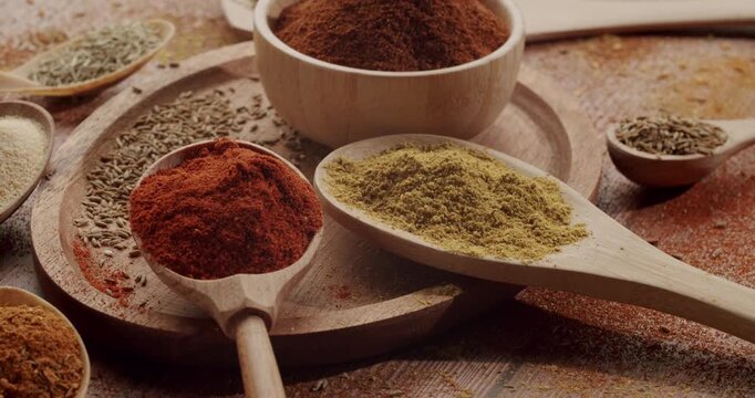 Various colorful and aromatic spices and herbs arranged in wooden bowls and spoons on a rustic table, highlighting traditional culinary ingredients and the richness of international cuisine