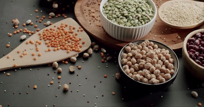 Colorful selection of raw uncooked legumes and grains displayed in bowls and spoons on a dark surface, Variety of colorful legumes and cereals in bowls rotating on a dark background.