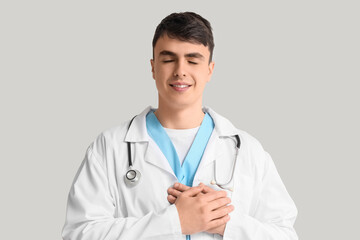 Fototapeta premium Male doctor keeping his hands on heart against light background