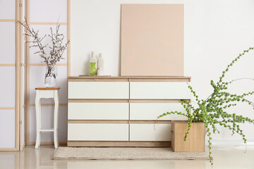 Interior of stylish room with dresser, folding screen and blooming tree branches