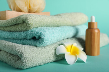 Stack of clean soft towels and flower on turquoise background, closeup