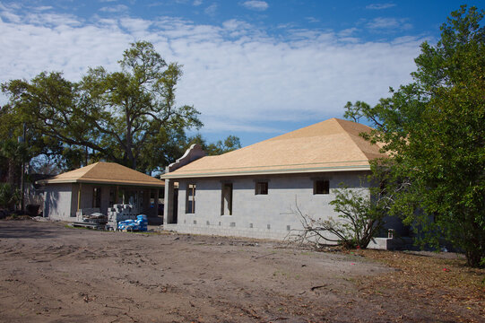 Unfinished concrete block house With Spanish-Style Parapets under construction with curved parapet facades, exposed wood framing and scattered building materials on a suburban lot beneath a blue sky, 