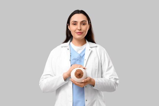 Female doctor with knitted breast model on light background