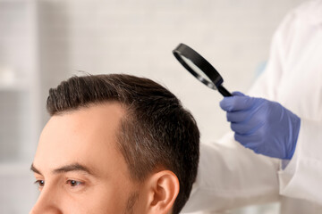 Fototapeta premium Trichologist with magnifier examining man's hair in clinic, closeup