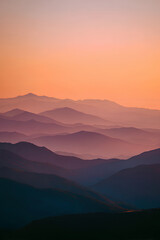 Obraz premium Layered Mountain Silhouettes at Sunset with Warm Orange Pink Gradient Sky Panoramic Serene Landscape