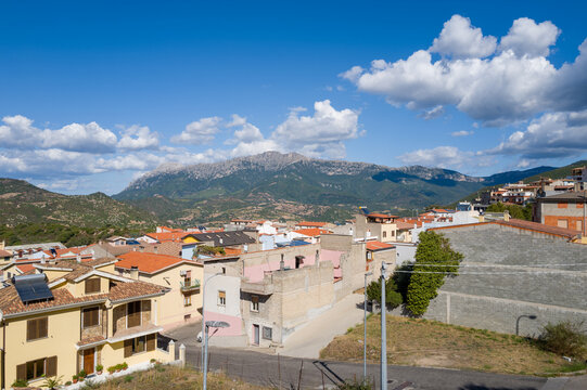 Colorful rooftops of Orgosolo town with rugged mountains and scattered clouds in the background under bright daylight in Sardinia.
