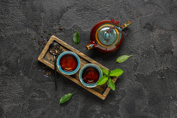 Naklejka premium Teapot with cups, spoon of dry tea and leaves on black grunge background