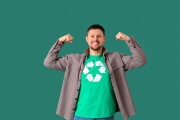 Happy young man in t-shirt with recycling logo showing muscles on green background. Ecology concept
