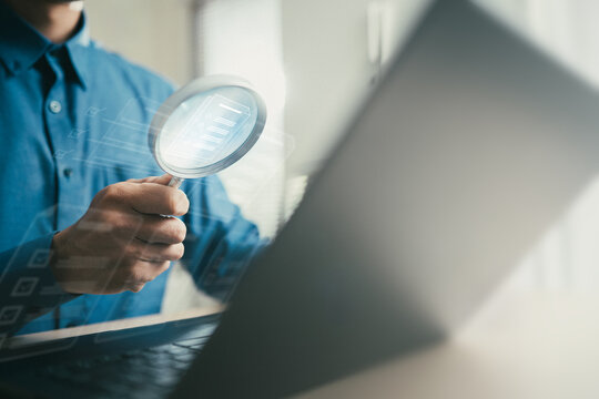 Business professional using magnifying glass to inspect digital documents on laptop. Concept of document management, internal audit, compliance review, data analysis, and financial report verification