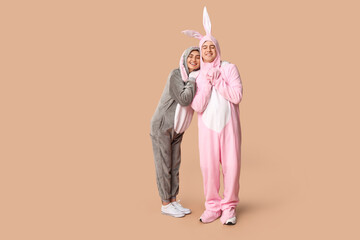 Fototapeta premium Beautiful young couple in bunny costume on brown background. Easter celebration