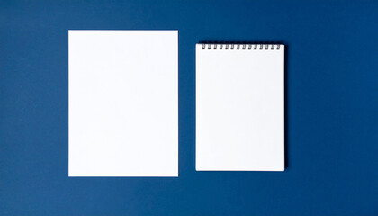 A4 paper and notepad on blue background viewed from above.