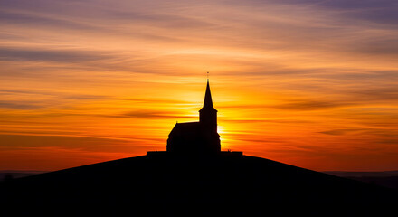 Silhouette of a church with a steeple on a hill against a vibran