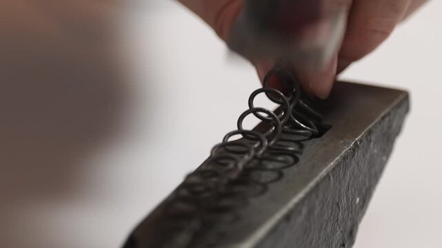 Close up of hammer shaping metal wire on anvil in traditional Slovak wire craft workshop. Drotarstvo handmade metalworking process and artisan craftsmanship detail.