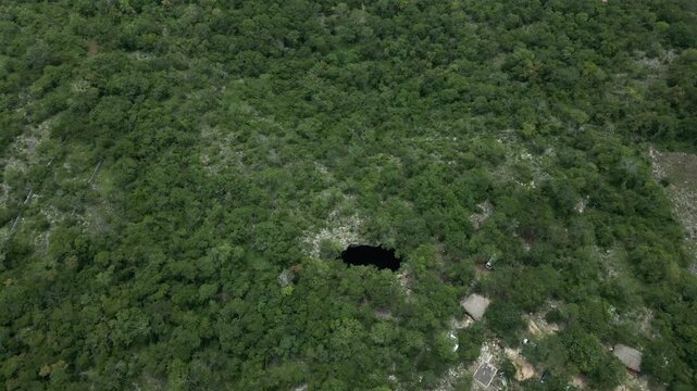 Cinematic aerial orbit over a deep black sinkhole (cenote) surrounded by lush green vegetation. Located near M&eacute;rida, Yucat&aacute;n, Mexico, this natural wonder is hidden in the dense Maya forest.