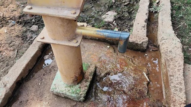 Orbiting shot of a rusty hand pump with water dripping onto stone base, wet concrete channel, mineral stains, rural ground textures, slow movement capturing decay life uv