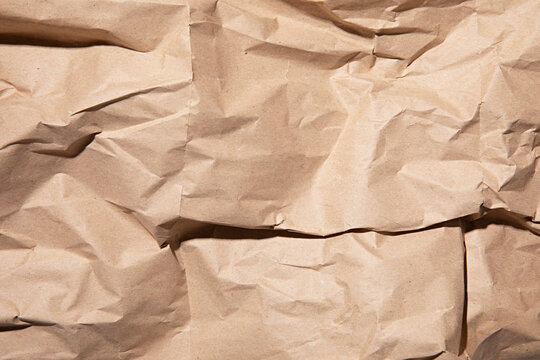 Close-up texture of crumpled brown kraft paper with dramatic shadows and highlights
