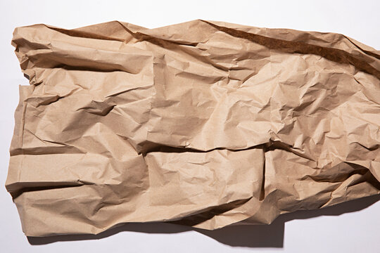 Close-up texture of crumpled brown kraft paper with dramatic shadows and highlights
