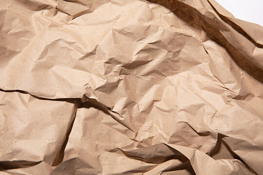 Close-up texture of crumpled brown kraft paper with dramatic shadows and highlights