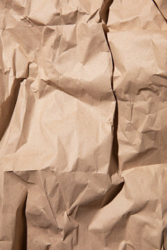 Close-up texture of crumpled brown kraft paper with dramatic shadows and highlights