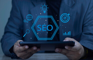 Businessman using tablet with SEO hologram and digital marketing icons: target, lightbulb, and chart. Concept of Search Engine Optimization strategy, web analytics, and online ranking.